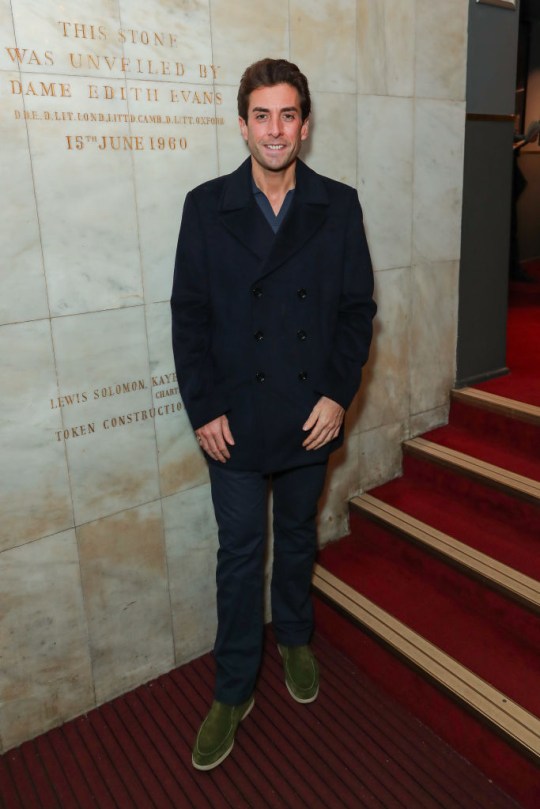 James Argent wearing a blue coat and trousers smiling while at a red carpet event