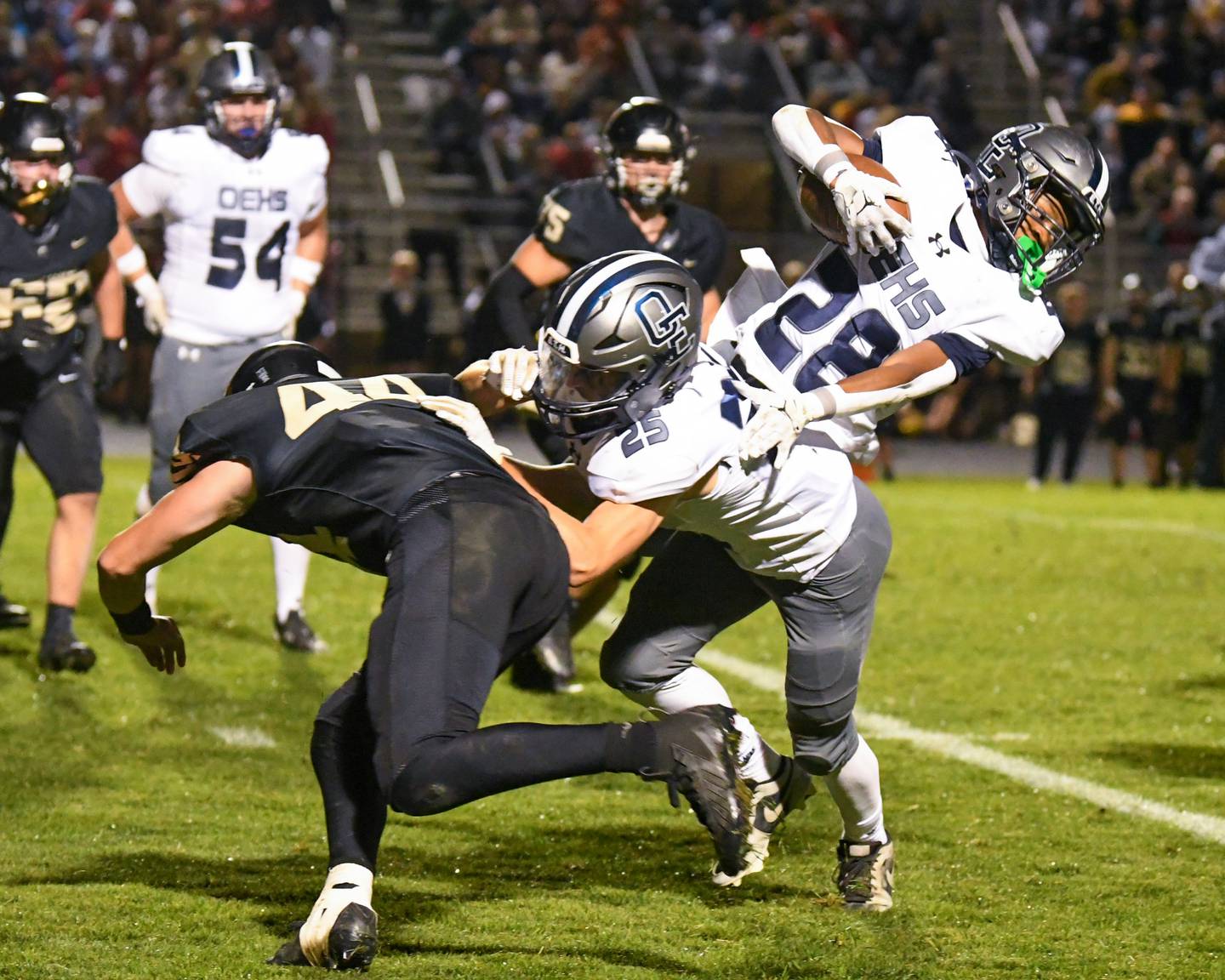 Oswego East's Aiden Fell, center, blocks Sycamore's Cooper Bode, as Oswego East's Zamarion Taylor (28) gains extra yards before being ruled down at the end of the play on Friday Sept. 6, 2024, during the game held at Sycamore High School.