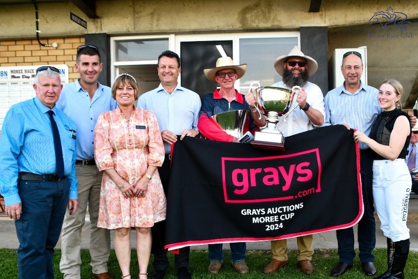 A team of equestrians hold a trophy and banner as they smile into the camera. 
