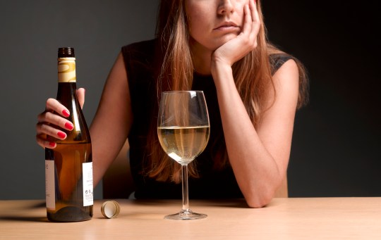 A white woman looks depressed while drinking a glass of white wine