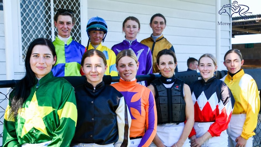 A group of female jockey's stand together smiling at the camera.