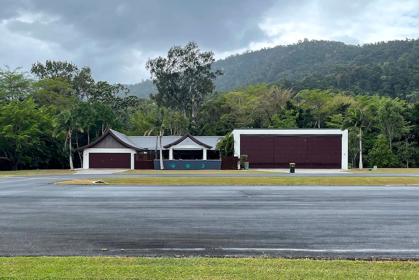 A house with a garage on the left and a large hanger on the right, with a concrete road in the foreground. 