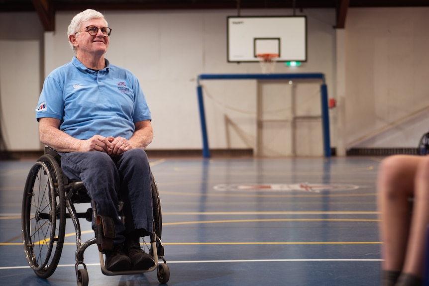 Man smiles in wheelchair looking up at basketball ring.