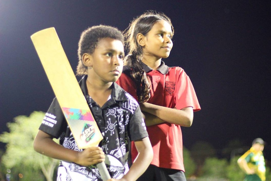 An indigenous boy and girl playing cricket at night